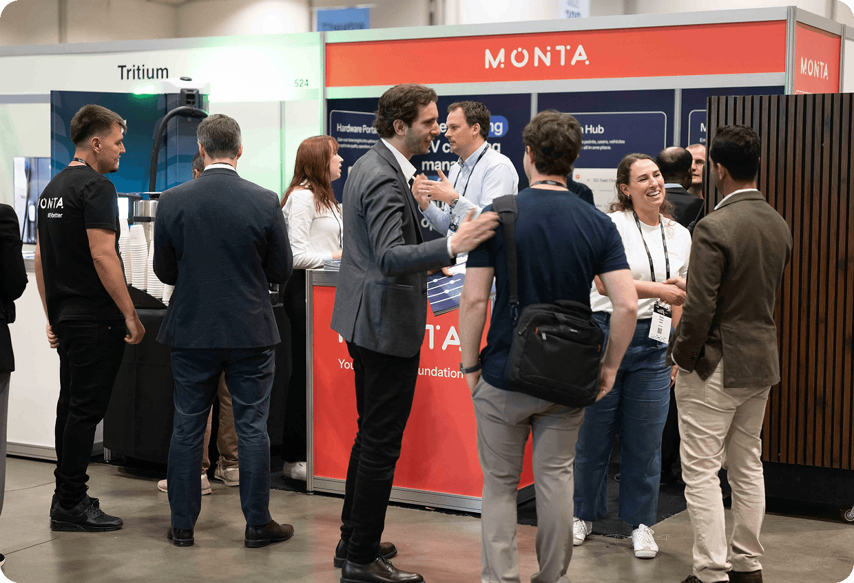 Monta's booth at a conference, featuring a red backdrop with the word "MONTA," attendees engaging and interacting around a coffee station.