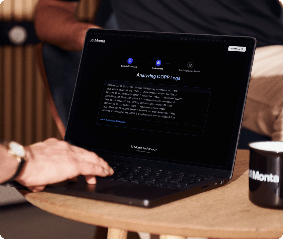 A person’s hand rests on a laptop displaying a dark screen with OCPP logs, beside a coffee cup featuring the Monta logo.